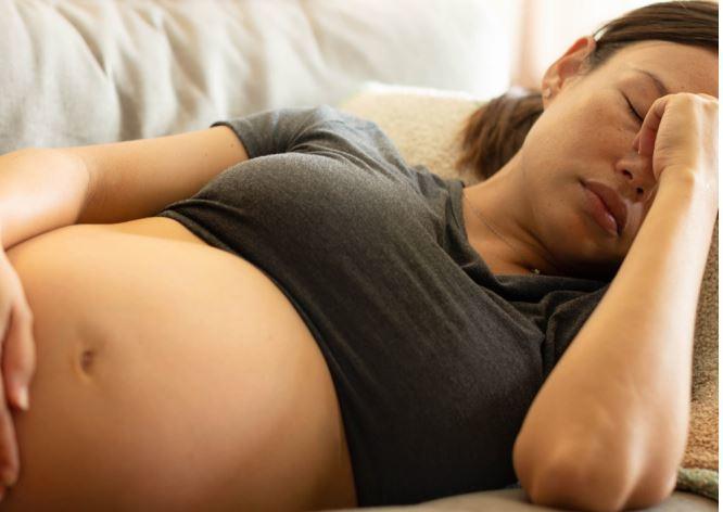 Pregnant woman laying on a couch with her eyes closed