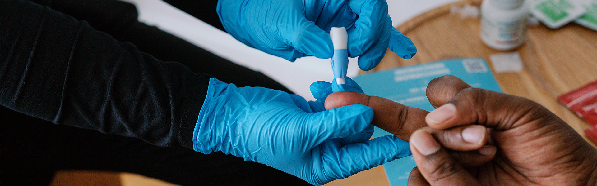 healthcare professional wearing glove pricks finger of patient