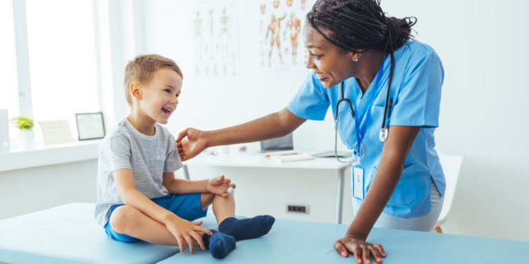 Smiling boy sits on exam table while talking with nurse