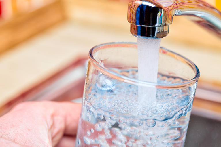 A hand holding a glass of water at the sink being filled. 